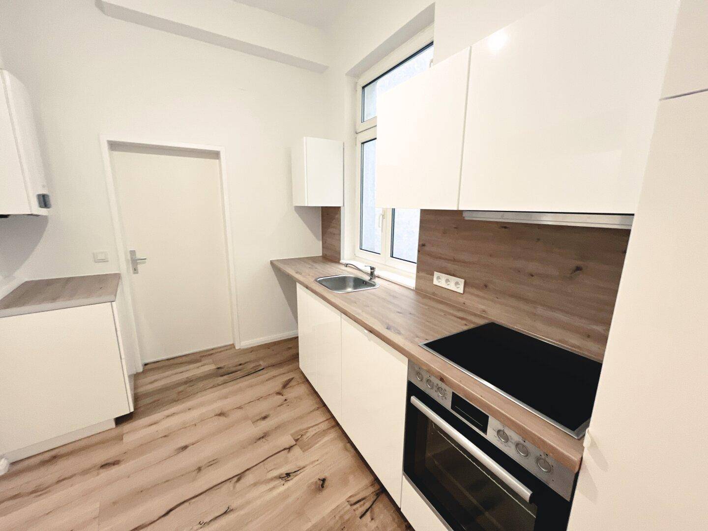 Moderne Einbauküche mit weißen Hochglanzfronten, Holzarbeitsplatte und integriertem Kochfeld und Backofen.