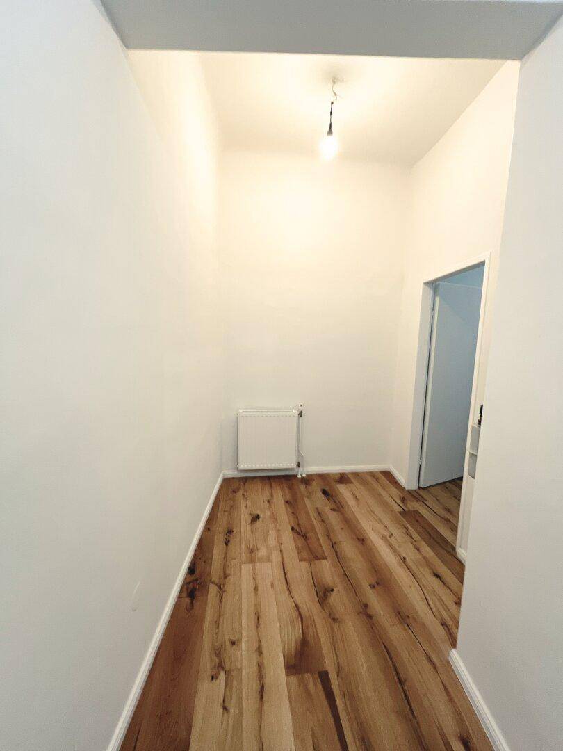 Langer, heller Flur mit Holzboden und weiß gestrichenen Wänden, der zu einem weiteren Raum führt.