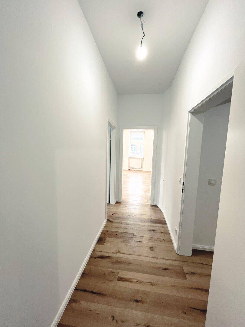 Langer, heller Flur mit Holzboden, der den Blick auf weitere Zimmer freigibt.