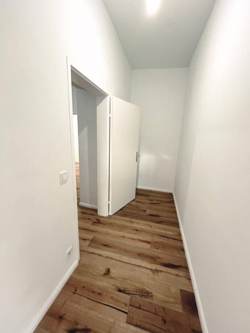 Schmaler Flur mit Holzboden und weißer Tür, die zu einem angrenzenden Raum führt.