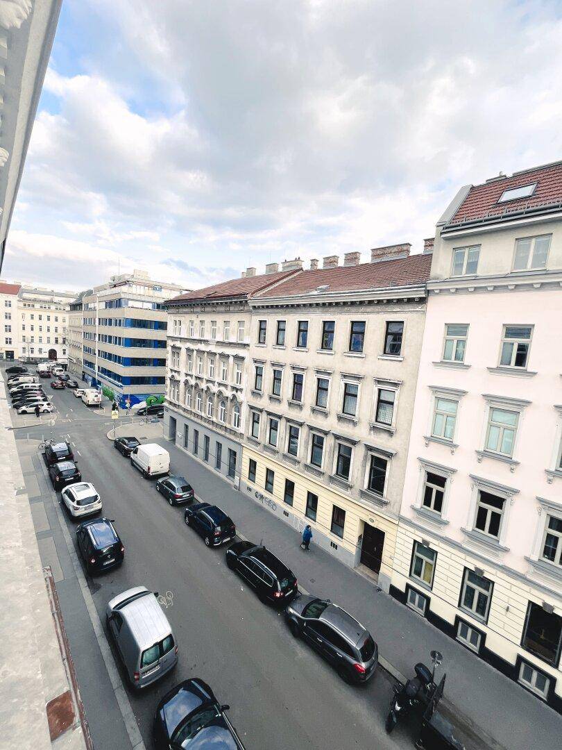 Blick von oben auf eine belebte Stadtstraße mit parkenden Autos und historischen Gebäuden.