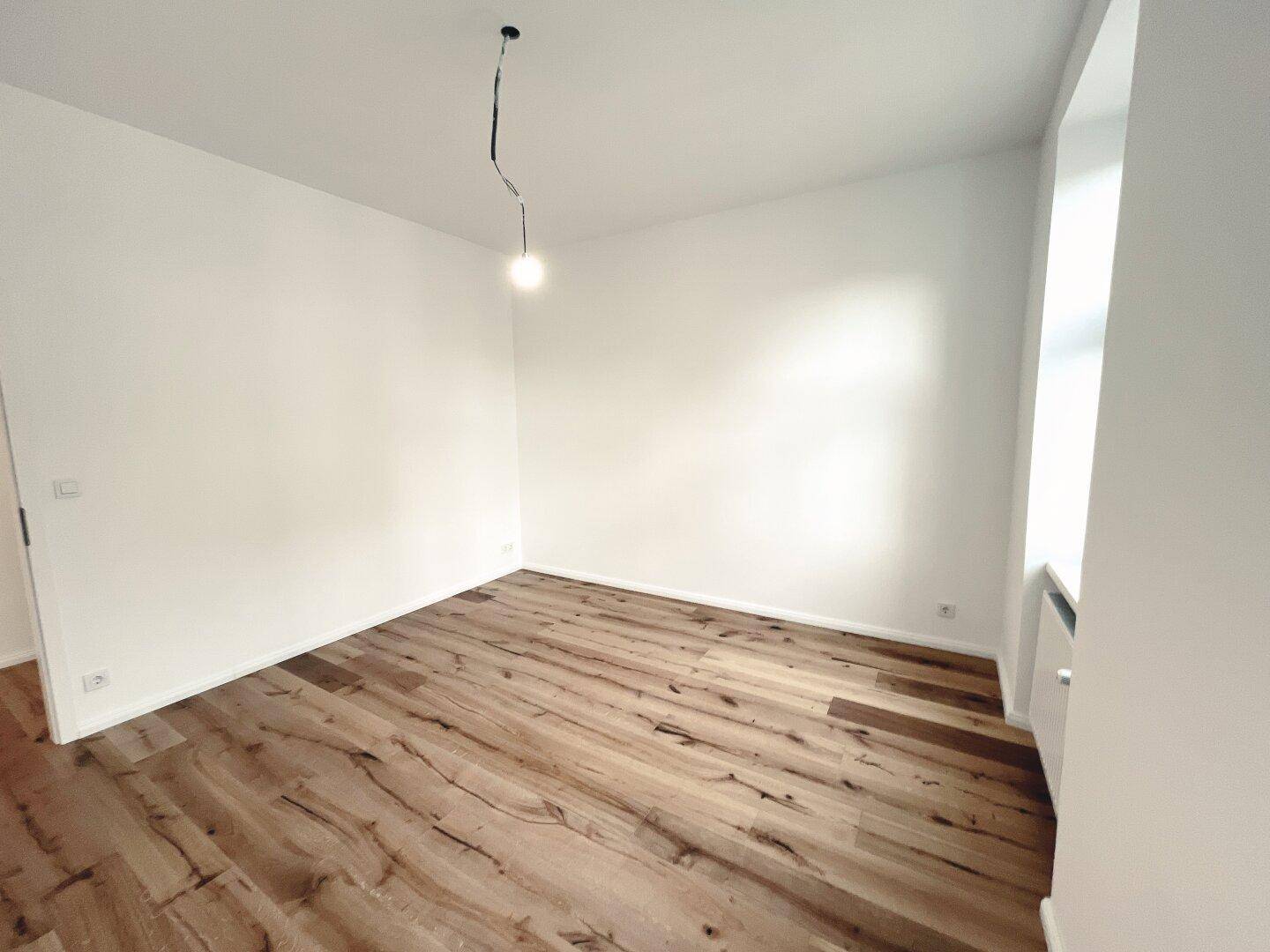 Geräumiges Zimmer mit Holzboden und viel Tageslicht, ideal für Schlaf- oder Arbeitsbereich.