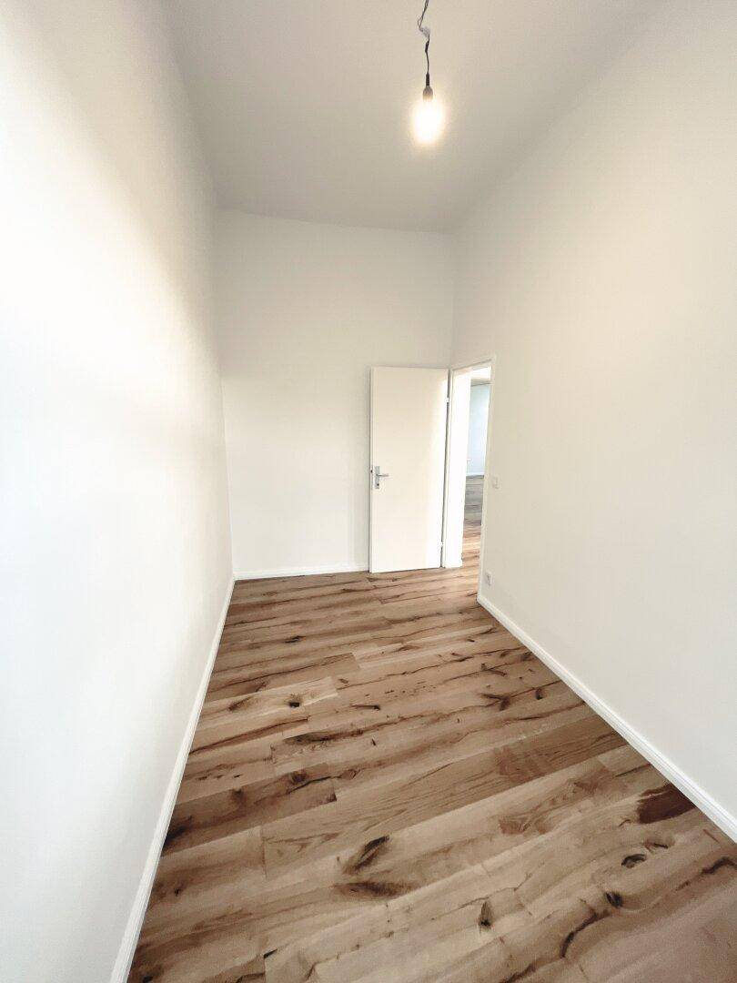 Schmaler Raum mit Holzboden und weiß gestrichenen Wänden, geeignet als kleines Schlafzimmer oder Büro.