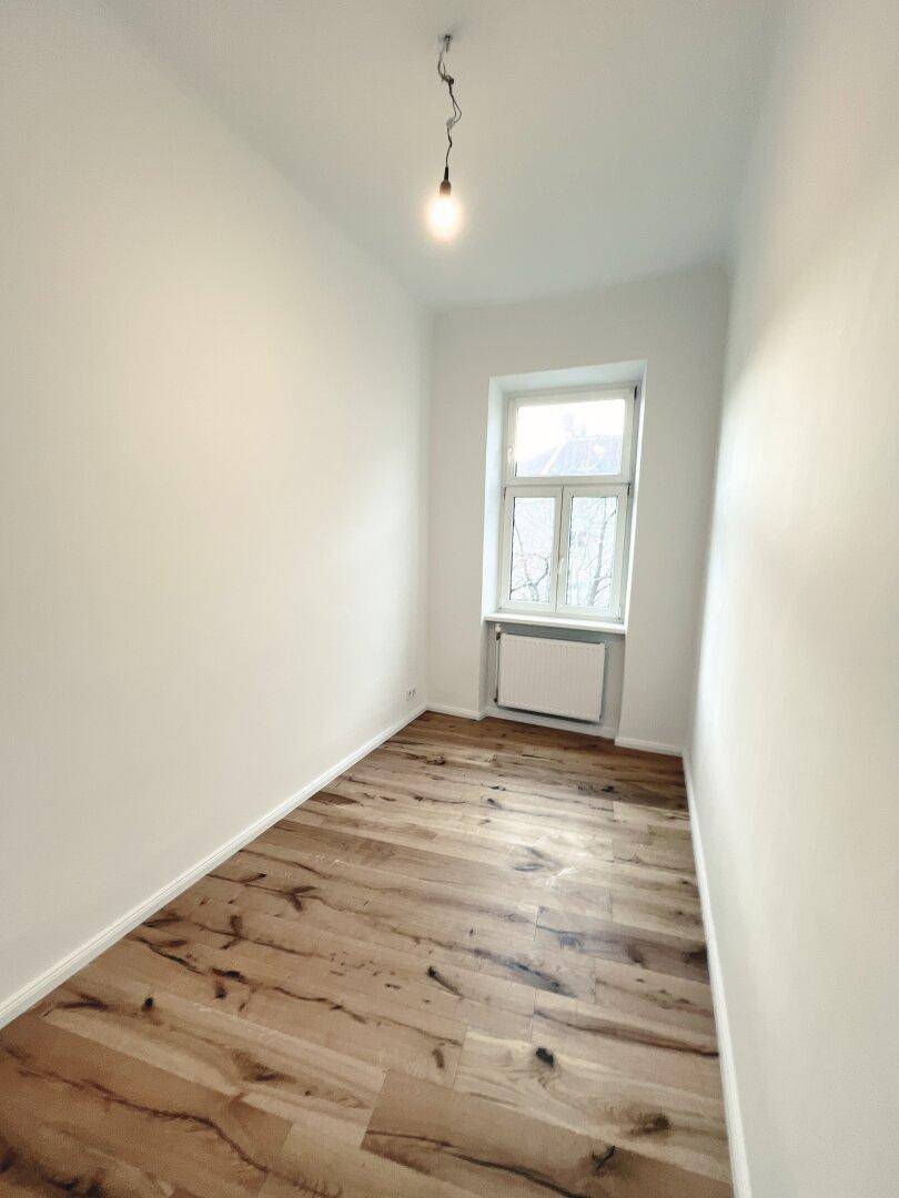 Helles Zimmer mit Fenster, Holzboden und weiß gestrichenen Wänden, in einem gepflegten Zustand.