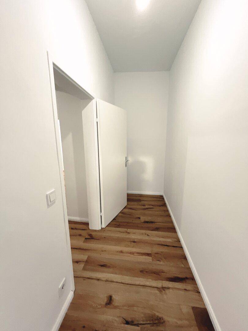 Schmaler Flur mit Holzboden und weißer Tür, die zu einem angrenzenden Raum führt.
