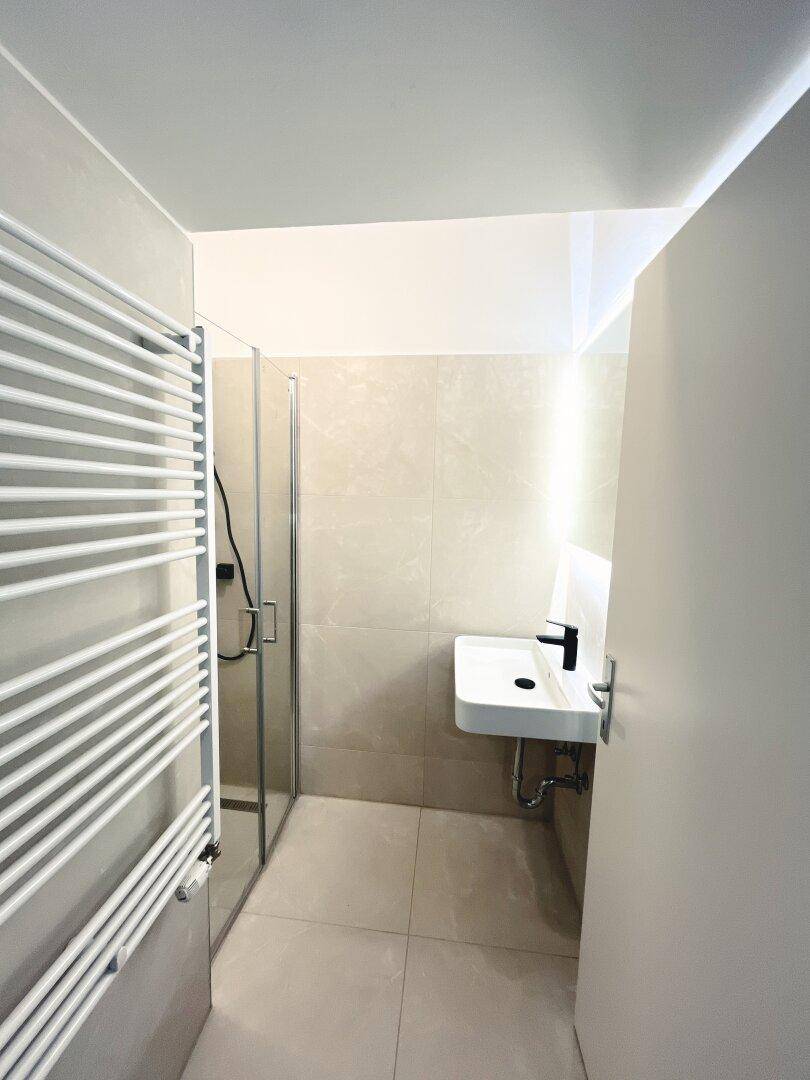 Modernes Badezimmer mit Duschkabine, Waschbecken und beheiztem Handtuchhalter.