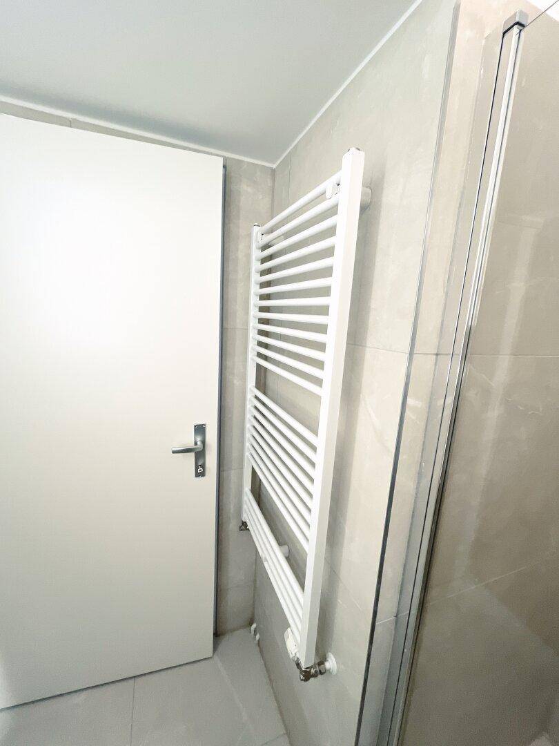 Beheizter Handtuchhalter in einem modernen Badezimmer mit hellen Fliesen und weißer Tür.