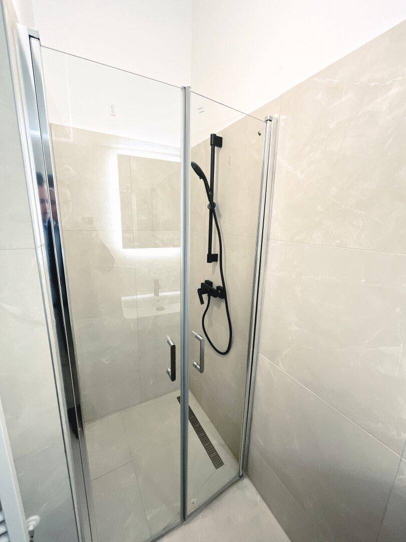 Modernes Badezimmer mit ebenerdiger Dusche, Glasabtrennung und hellen Fliesen.