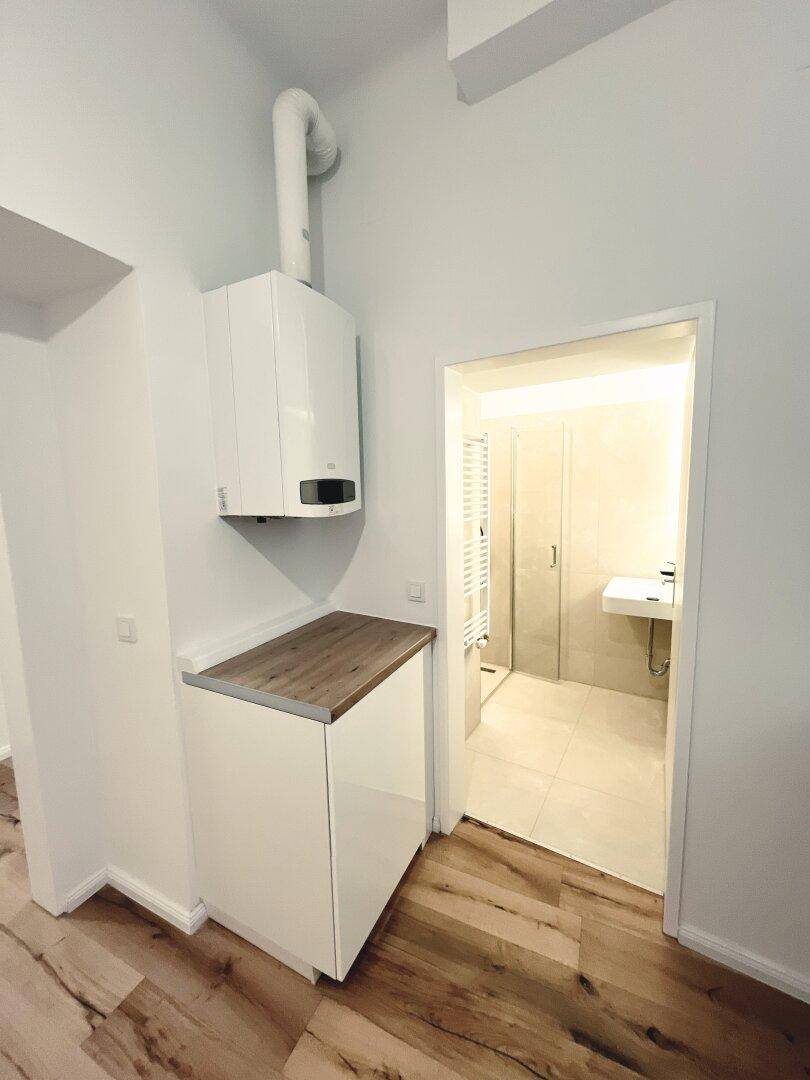 Küchenbereich mit Heiztherme, weißen Schränken und Zugang zu einem modernen Badezimmer.