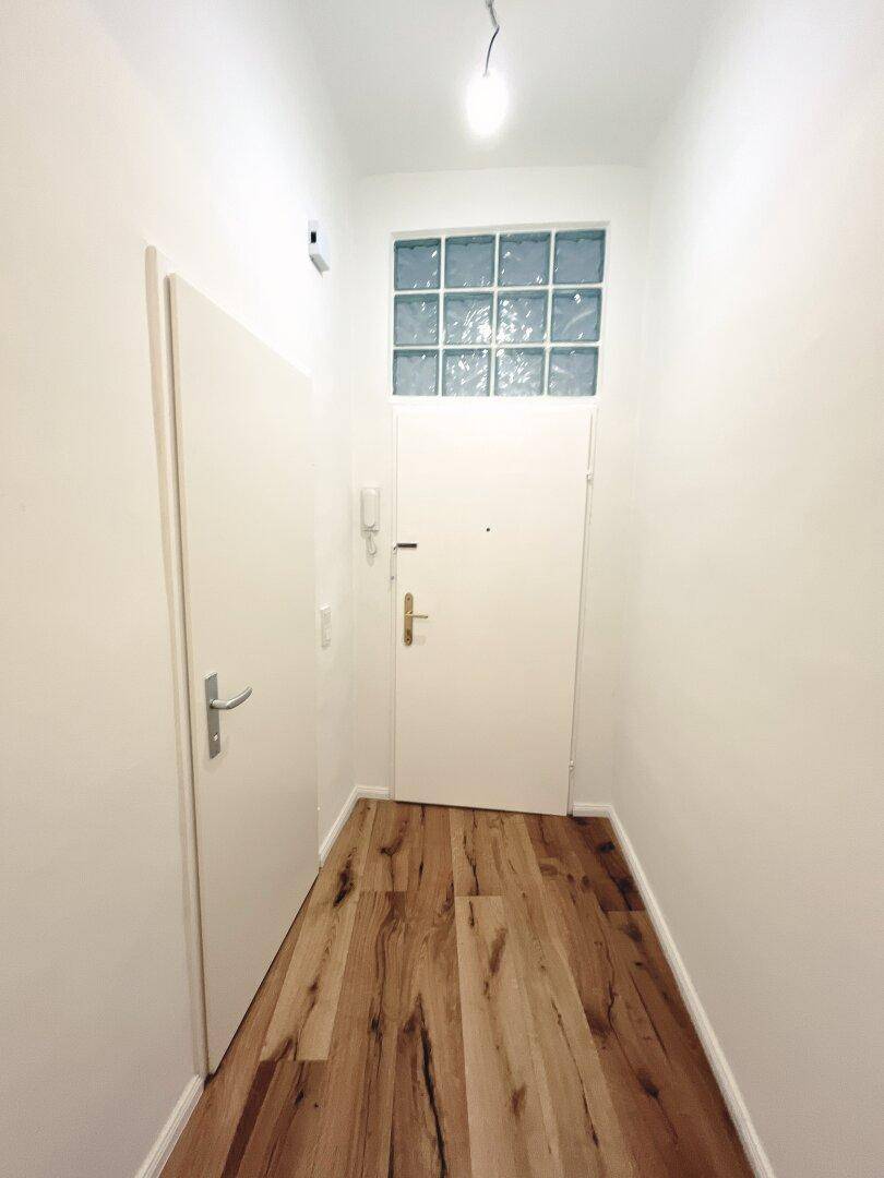 Heller Eingangsbereich mit Holzboden und einer Tür mit Glasbaustein-Oberlicht.