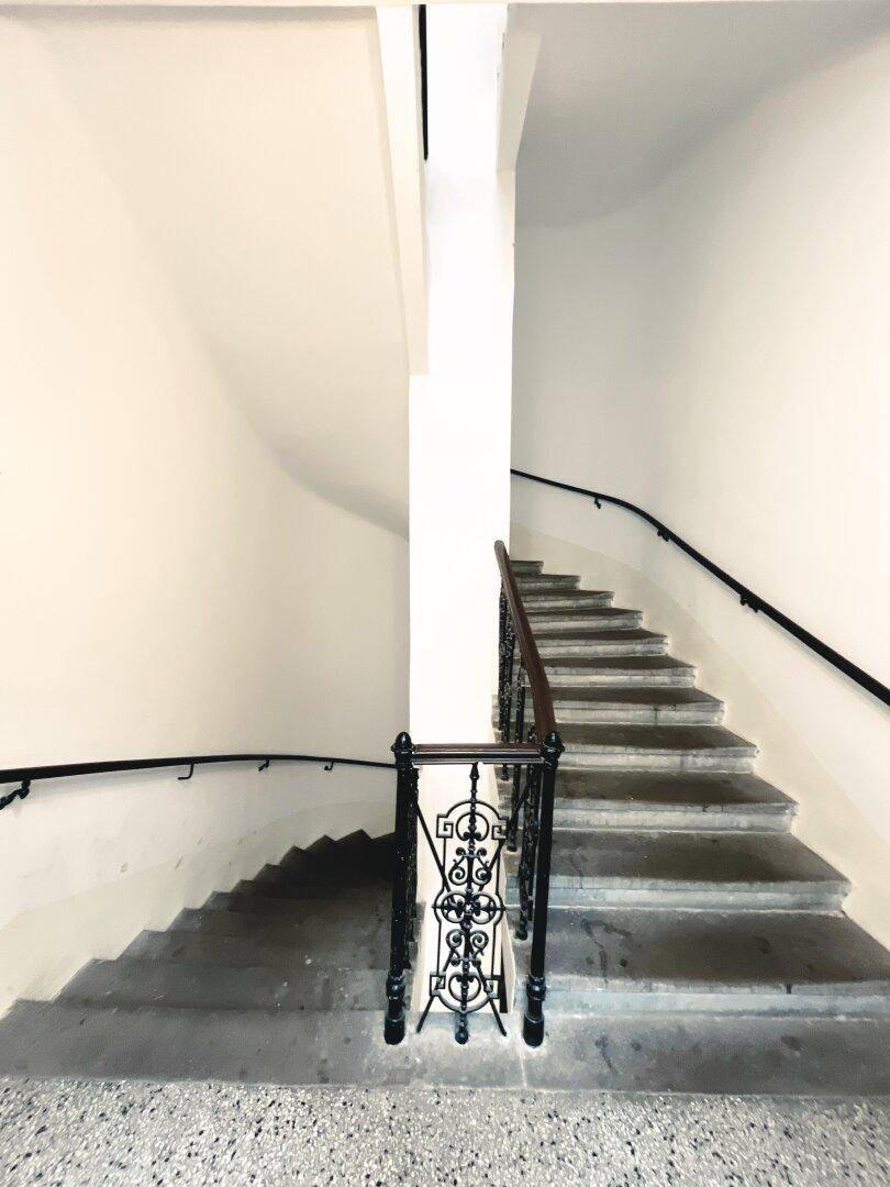 Historisches Treppenhaus mit Steinstufen und schmiedeeisernem Geländer in einem Altbau.