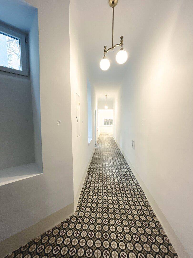 Langer, eleganter Hausflur mit gemusterten Fliesen, Stuckelementen und klassischer Deckenleuchte.