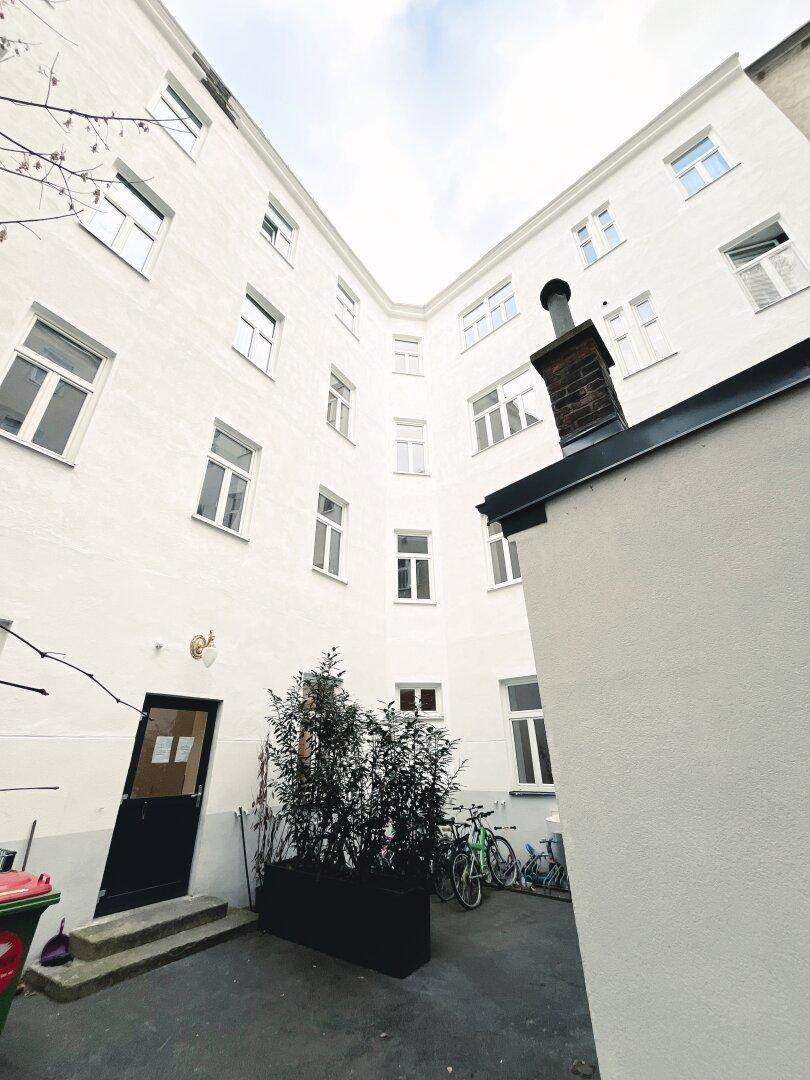 Innenhof eines Wohngebäudes mit weißer Fassade, Fenstern und Fahrradabstellmöglichkeiten.