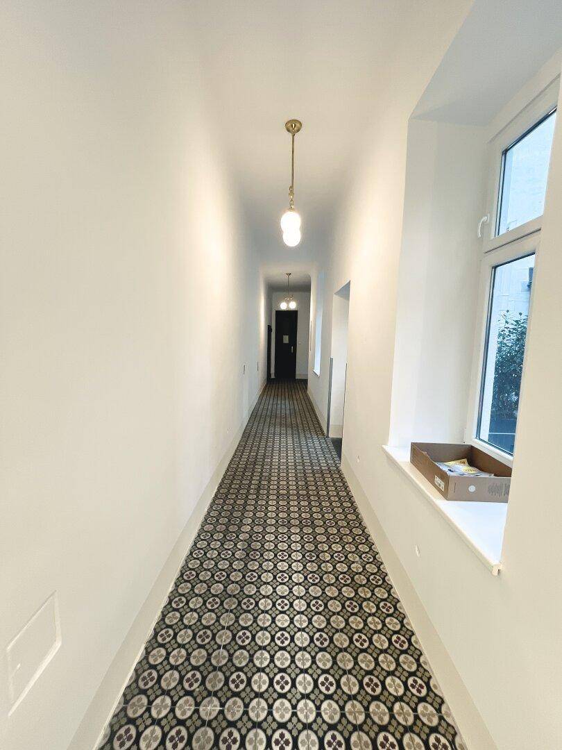 Langer, eleganter Hausflur mit gemusterten Fliesen, Stuckelementen und klassischer Deckenleuchte.