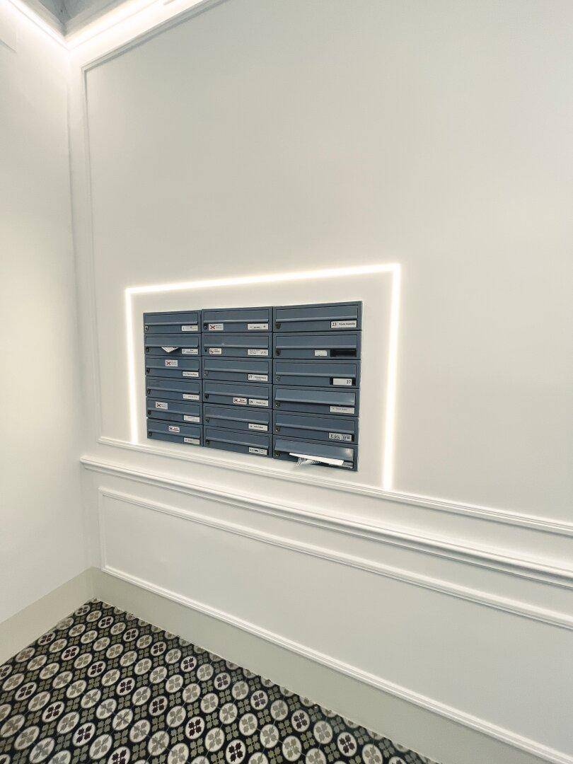 Moderner Eingangsbereich mit Briefkästen, beleuchteter Wandverkleidung und gemustertem Fliesenboden.
