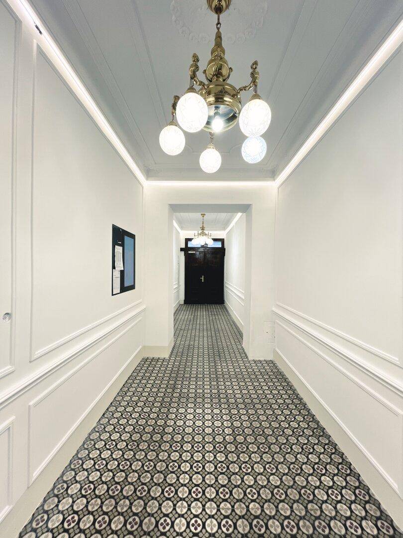 Langer, eleganter Hausflur mit gemusterten Fliesen, Stuckelementen und klassischer Deckenleuchte.