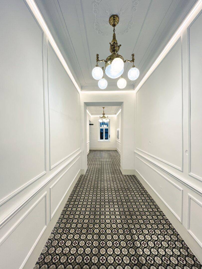 Langer, eleganter Hausflur mit gemusterten Fliesen, Stuckelementen und klassischer Deckenleuchte.