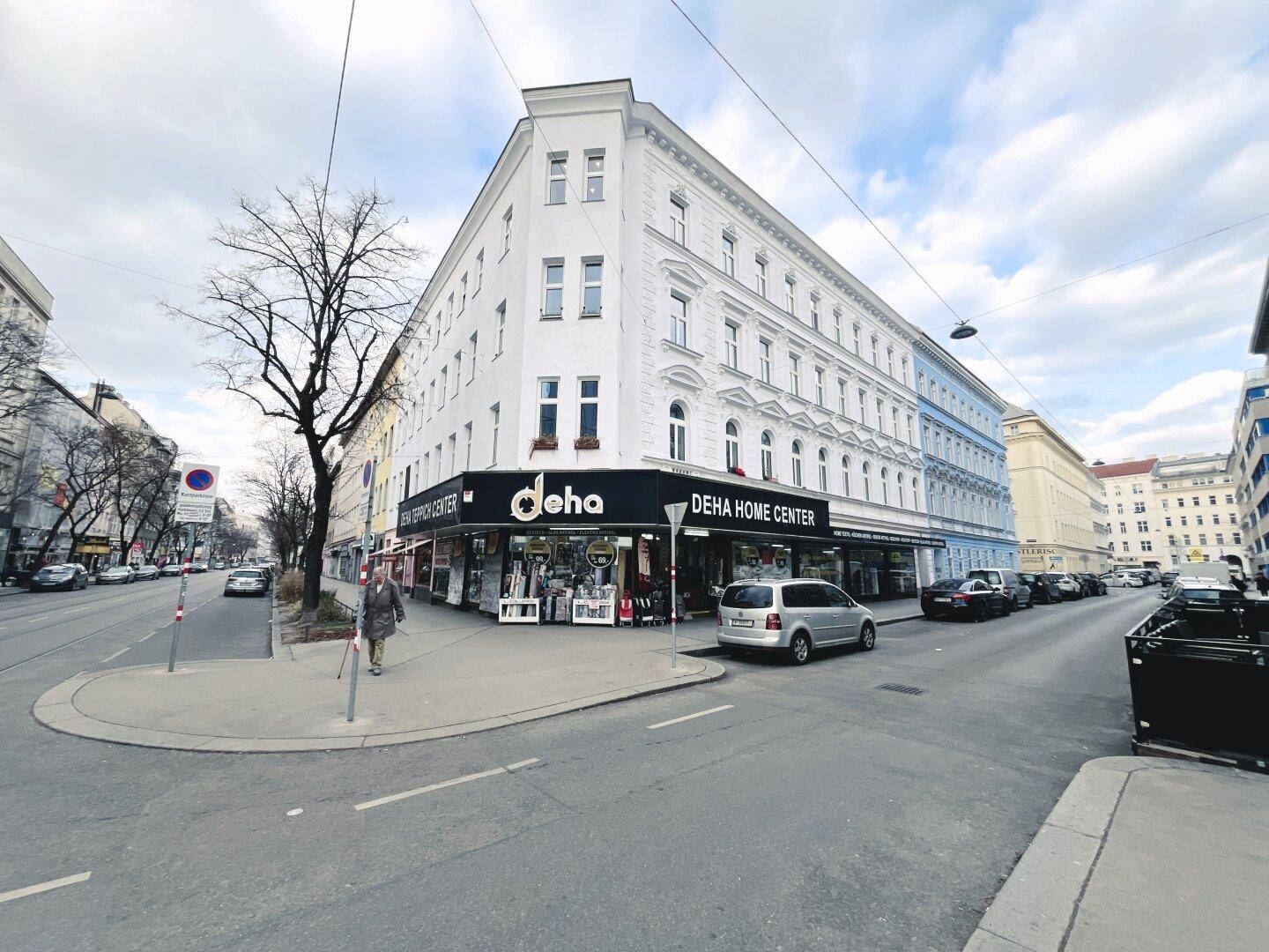 Eckgebäude mit weißer Fassade und Geschäften im Erdgeschoss an einer städtischen Kreuzung.