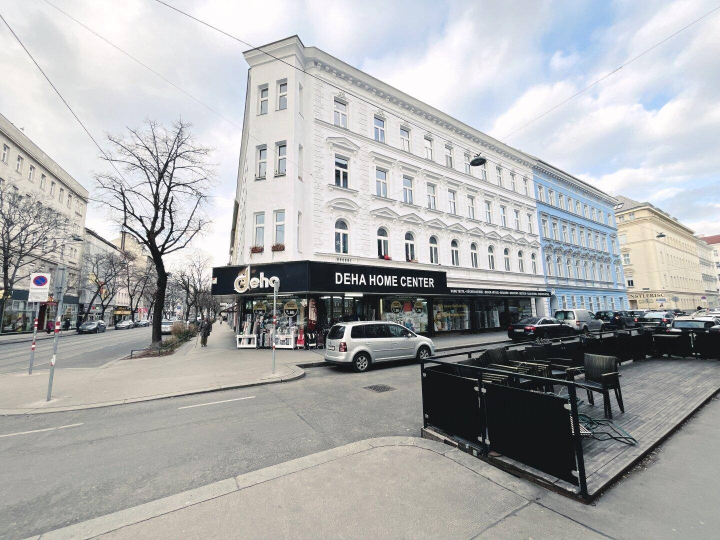 Eckgebäude mit weißer Fassade und Geschäften im Erdgeschoss an einer städtischen Kreuzung.