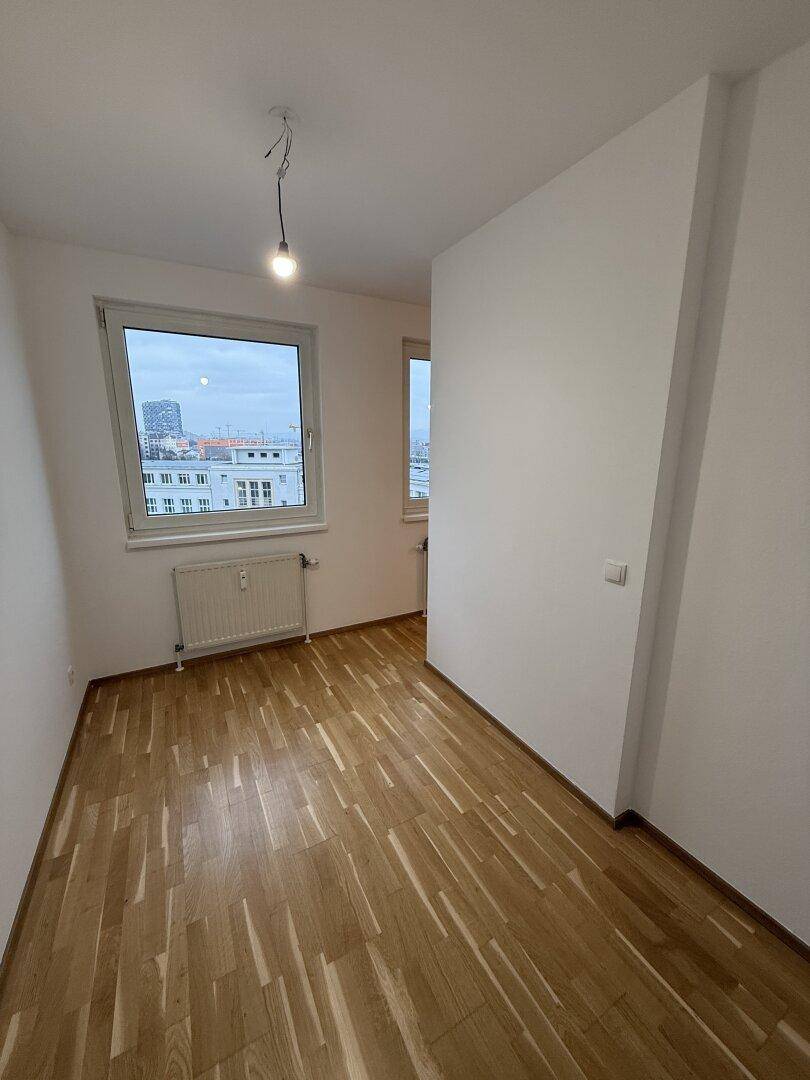 Helles Schlafzimmer mit Parkettboden und einem großen Fenster, das viel Tageslicht hereinlässt.