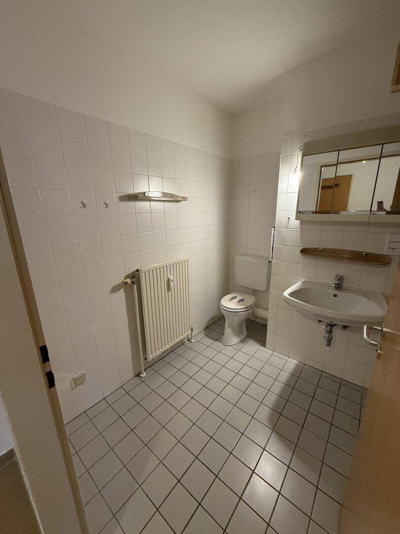 Kleines WC mit weißen Fliesen, Waschbecken, Toilette und Heizkörper.