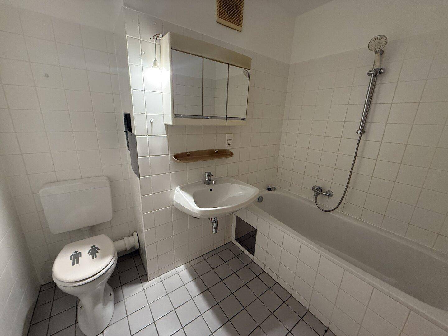 Badezimmer mit weißen Fliesen, Badewanne, Waschbecken und Toilette, in gutem Zustand.