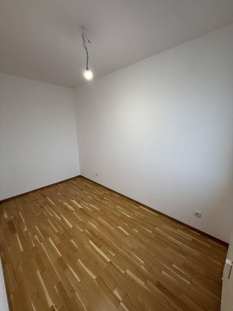 Leeres Zimmer mit Parkettboden und weißen Wänden, bereit für die Einrichtung.