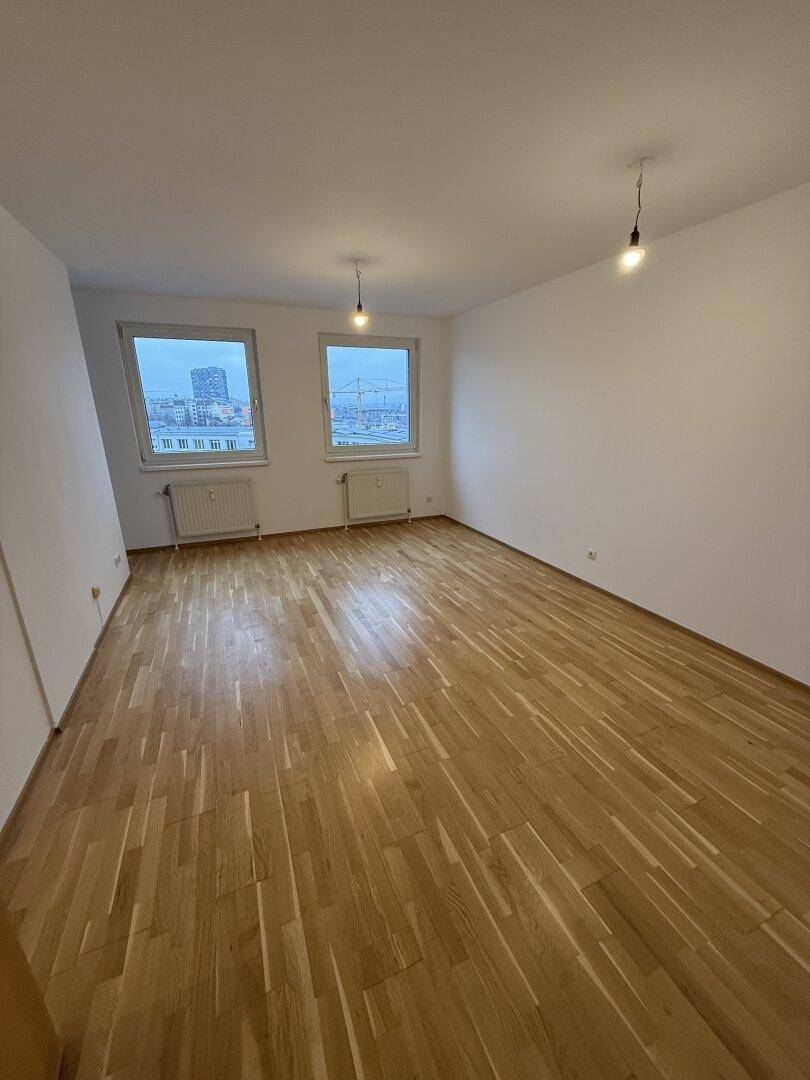 Großes, helles Zimmer mit Parkettboden und zwei Fenstern, die viel Tageslicht hereinlassen.