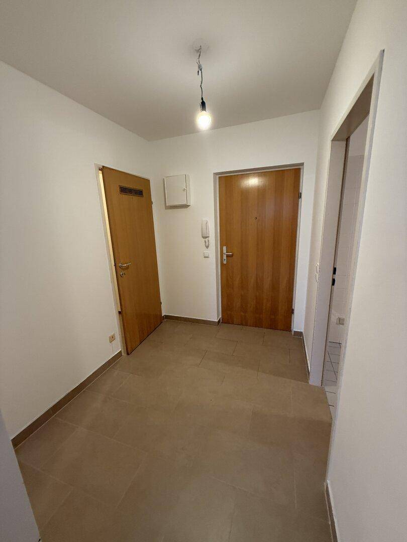Heller Eingangsbereich mit Fliesenboden und Holztüren, der zu den Wohnräumen führt.