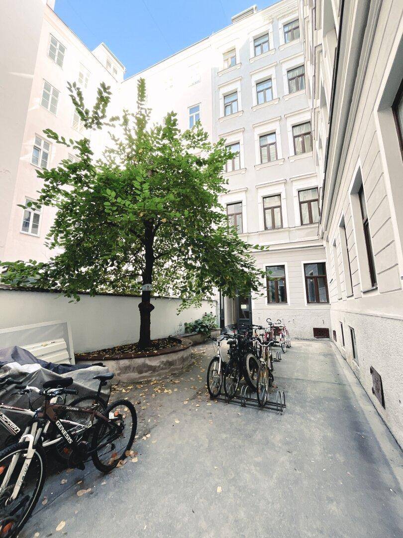 Grüner Innenhof mit Fahrradstellplätzen und einem Baum, umgeben von Gebäuden.