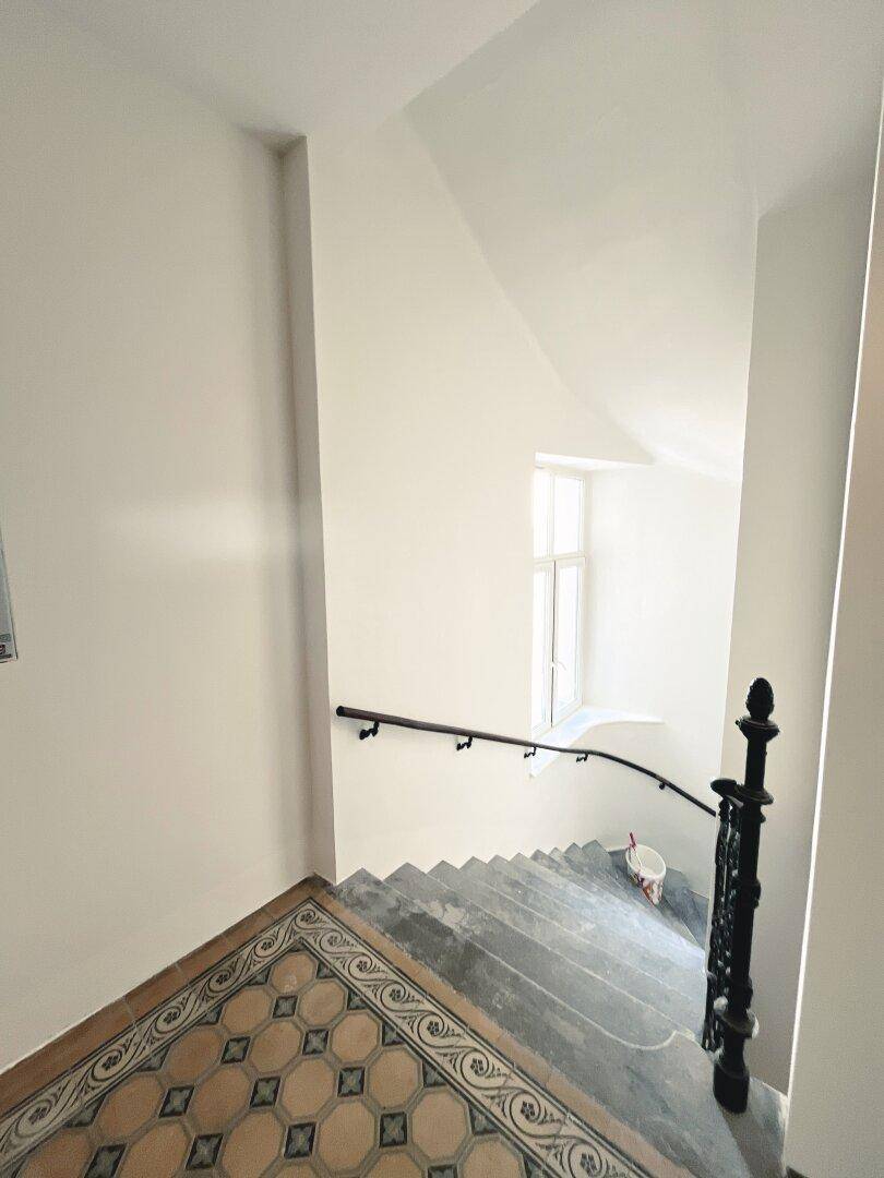 Historisches Treppenhaus mit gemusterten Fliesen und schmiedeeisernem Geländer.