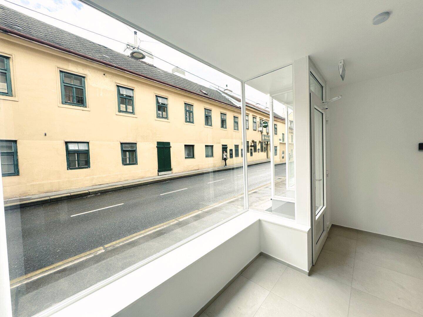 Weitläufige Fensterfront eines Ladenlokals mit umfassendem Blick auf die belebte Straße und historische Gebäude.
