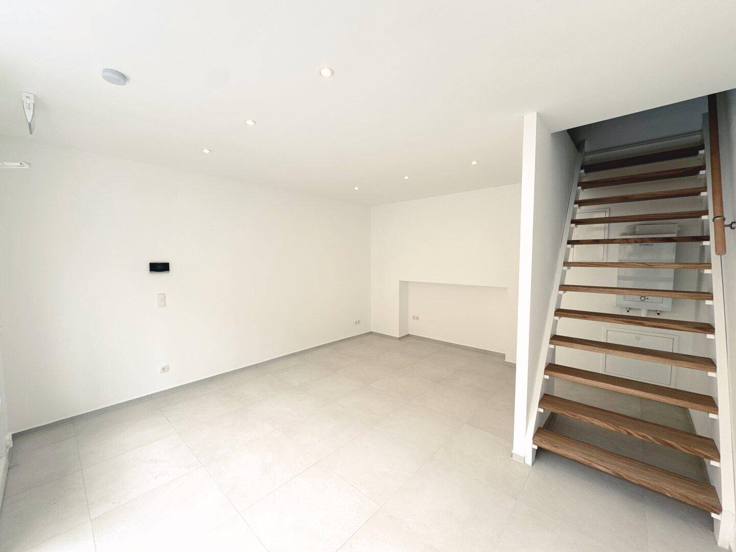 Geräumiger, heller Geschäftsraum mit moderner Holztreppe und Einbaustrahlern in der Decke.