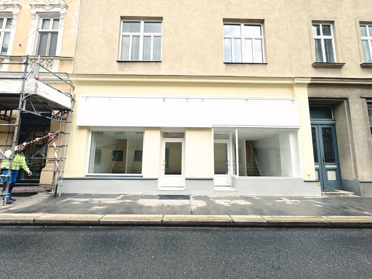Außenansicht eines Geschäftsgebäudes mit großen Schaufenstern und zwei Eingängen an einer Straße.