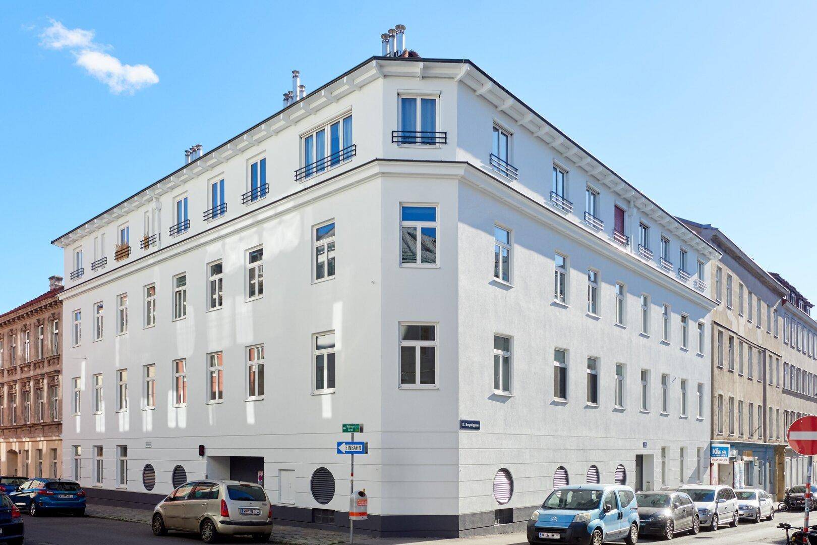 Modernes Eckgebäude mit weißer Fassade und vielen Fenstern in städtischer Umgebung.