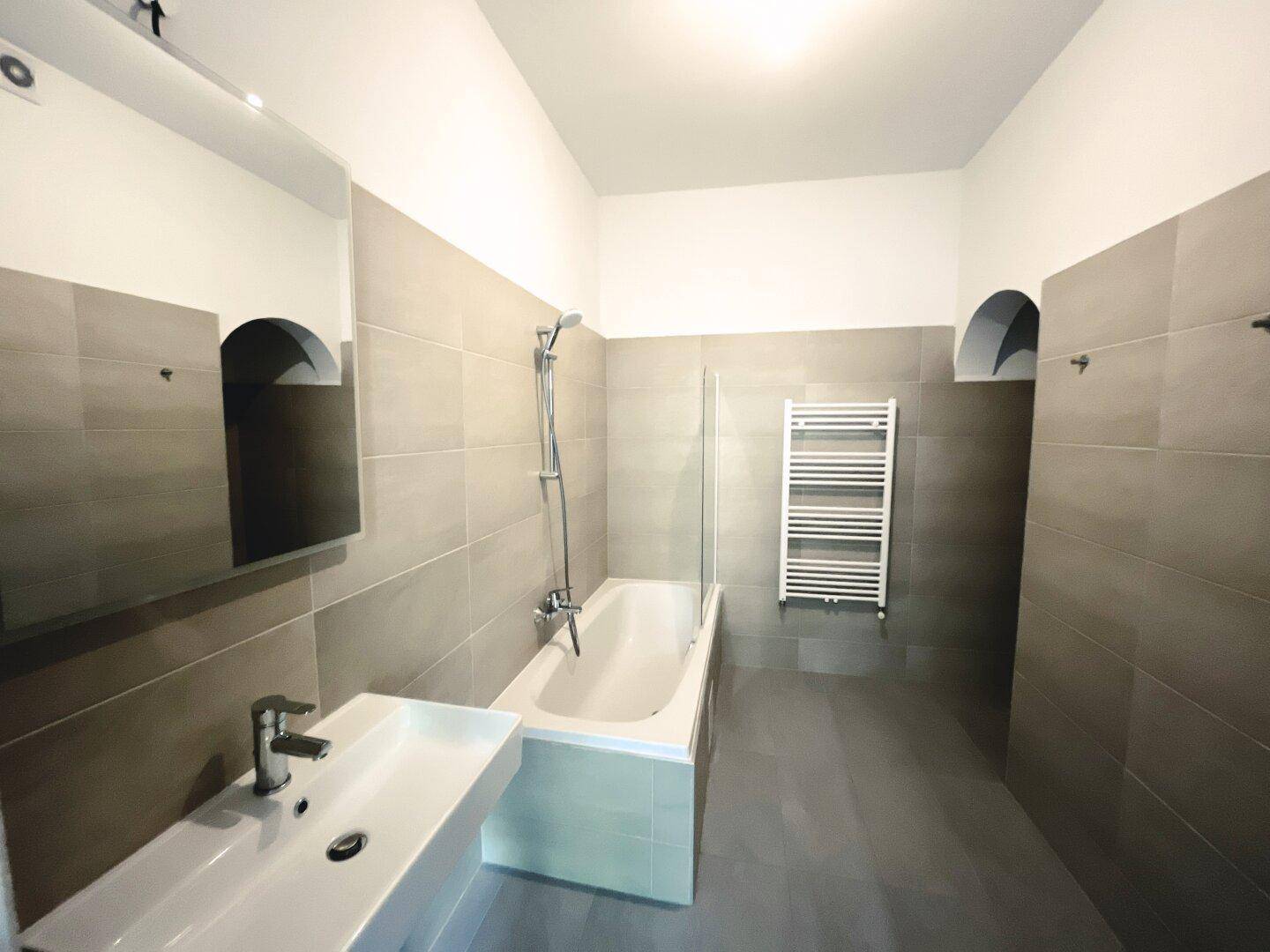 Modernes Badezimmer mit Badewanne, Waschbecken und beheiztem Handtuchhalter in neutralen Fliesen.