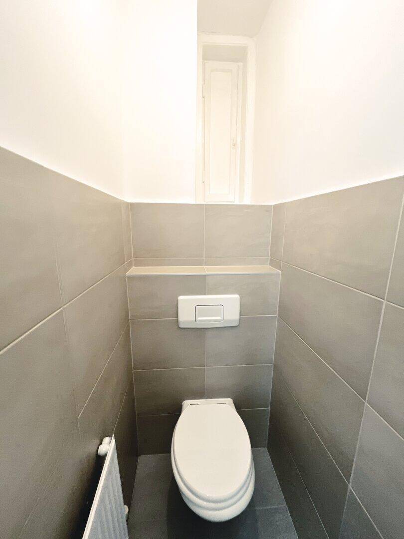 Separates WC mit Wand-WC und modernen grauen Fliesen, funktional und sauber gestaltet.