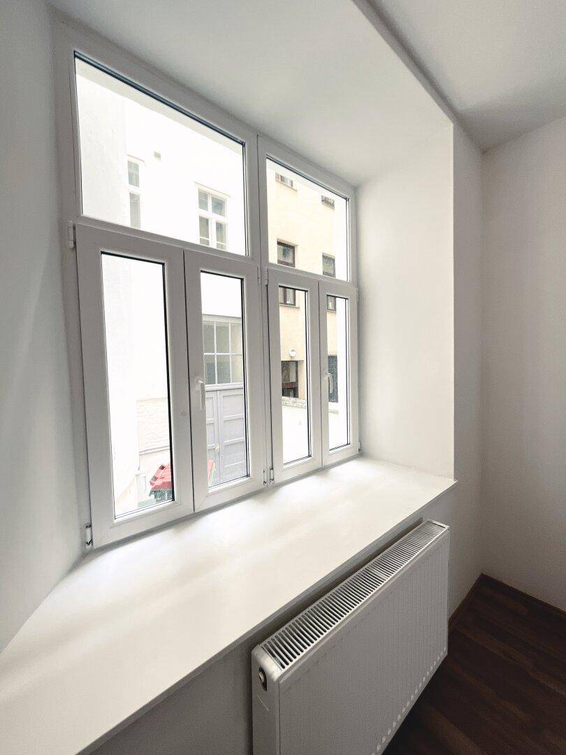 Großes Fenster mit breiter Fensterbank und Heizkörper, bietet Blick auf die umliegenden Gebäude.