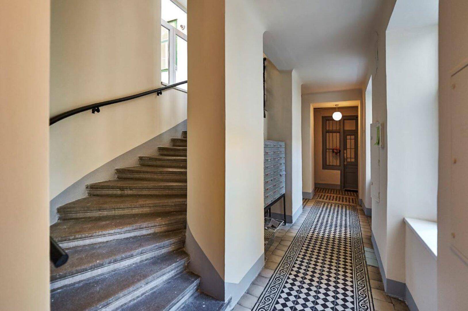 Heller Flur mit Steintreppe und Schachbrettmuster-Fliesenboden, führt zu weiteren Räumen.
