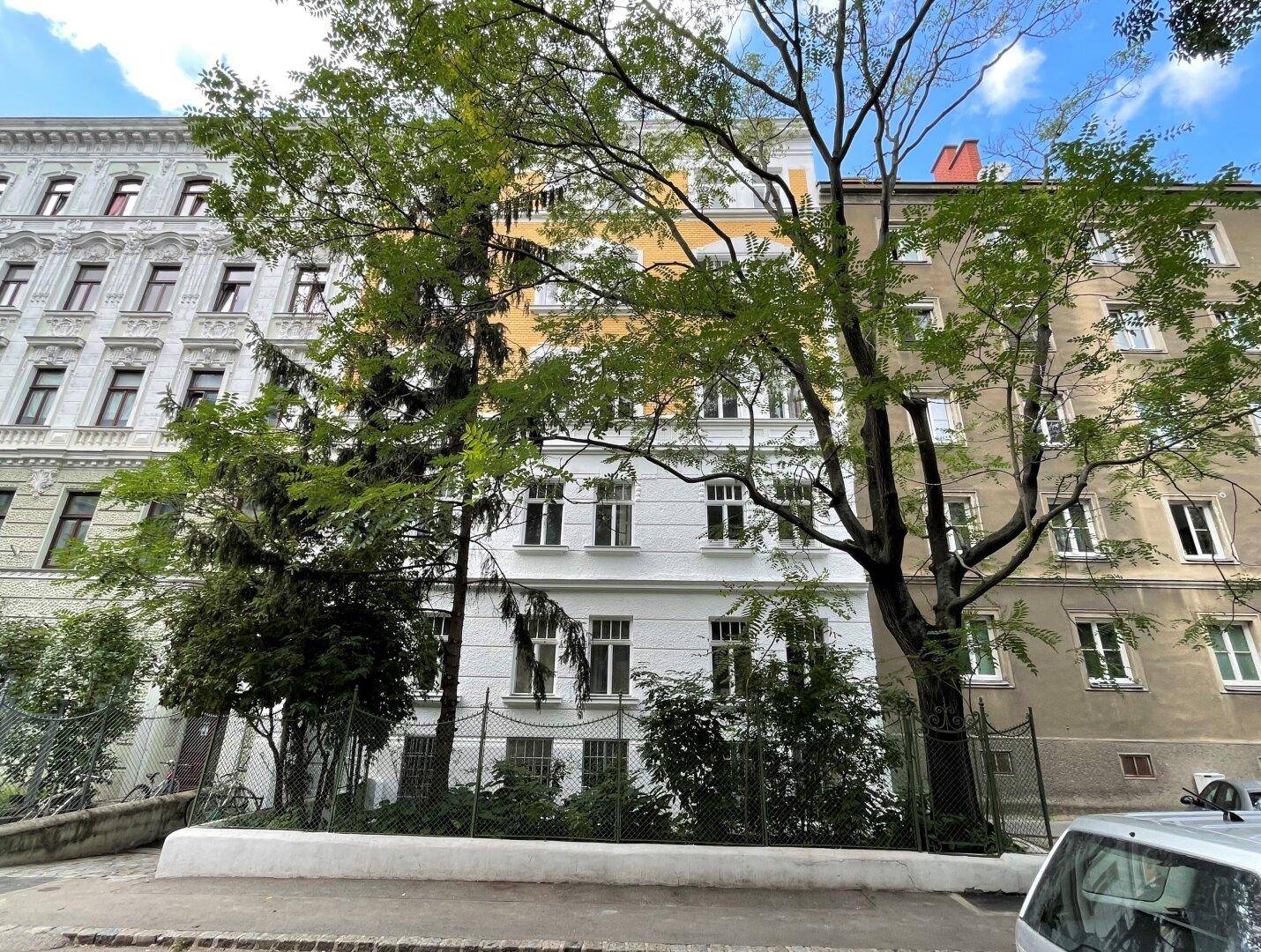 Historische Wohngebäude mit grünen Bäumen davor, typisch für eine städtische Umgebung.