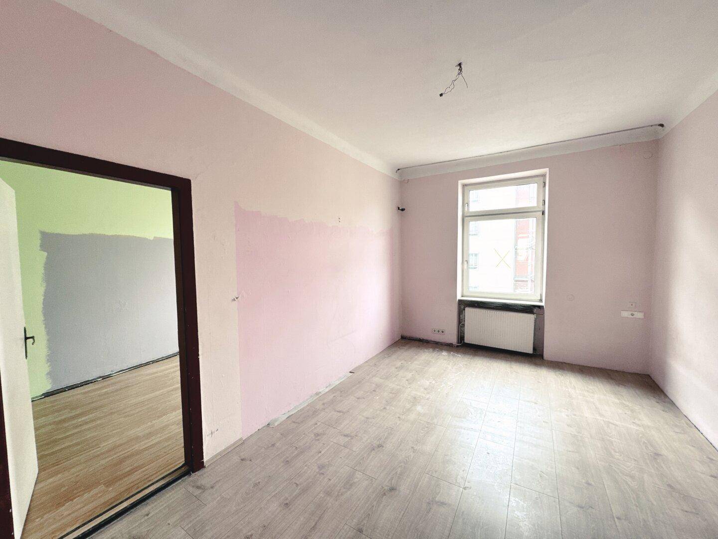 Leeres Zimmer mit rosa gestrichenen Wänden und hellem Laminatboden, bereit zur Renovierung.