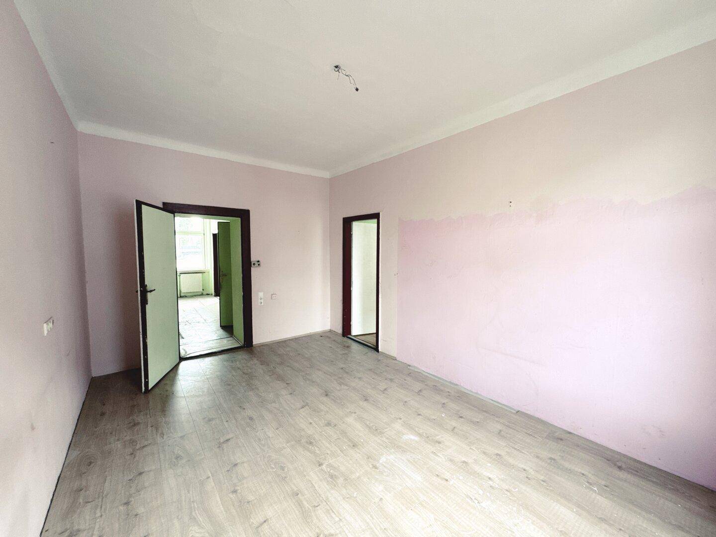 Geräumiges Zimmer mit rosa Wänden und Laminatboden, bietet Zugang zu weiteren Räumen.