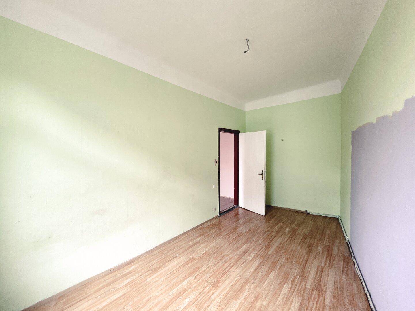 Leeres Zimmer mit grünen Wänden und Laminatboden, bietet Zugang zu einem weiteren Raum.