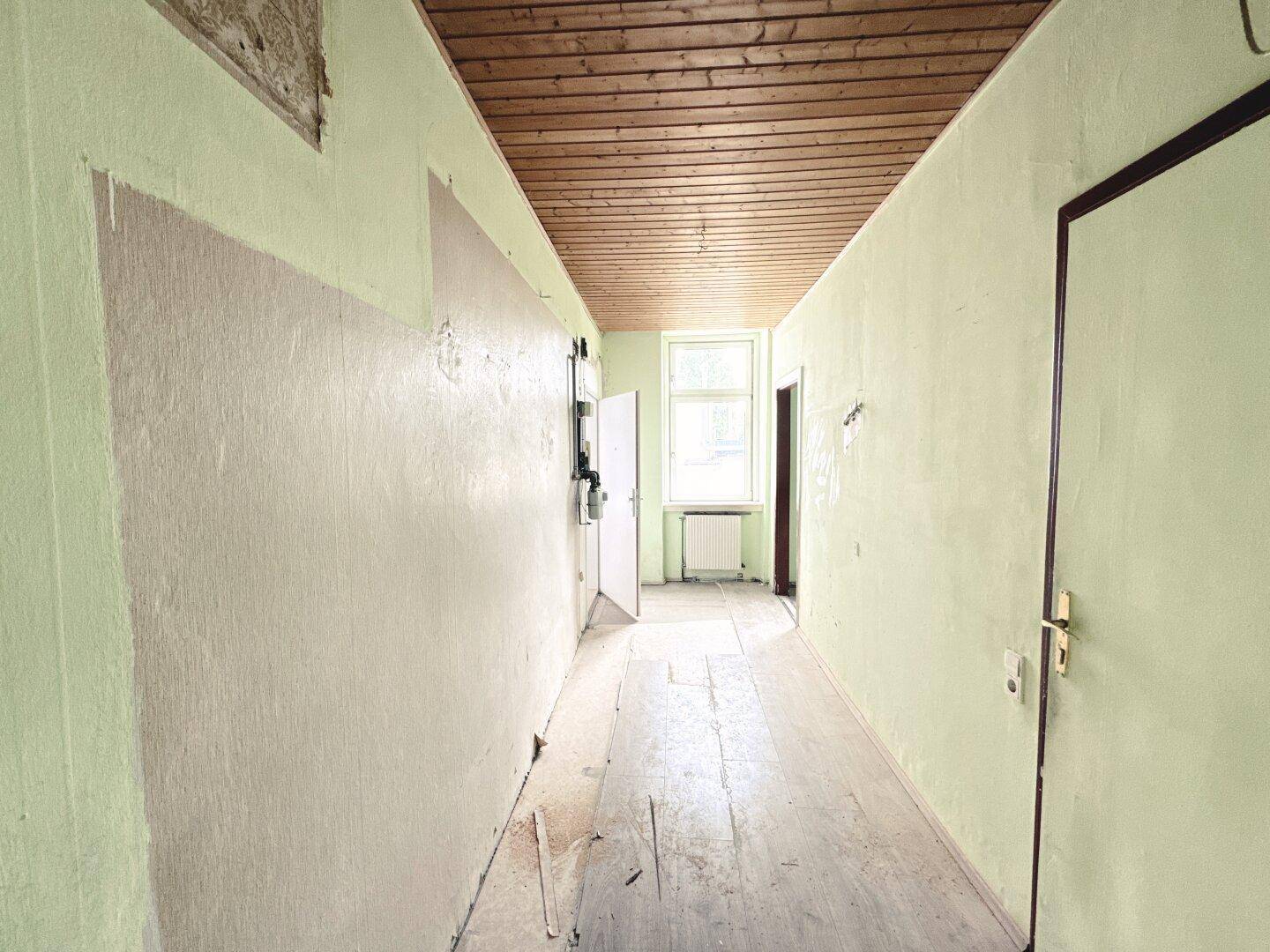 Langer Flur mit Holzdecke und alten Dielenböden, der auf eine Renovierung wartet.