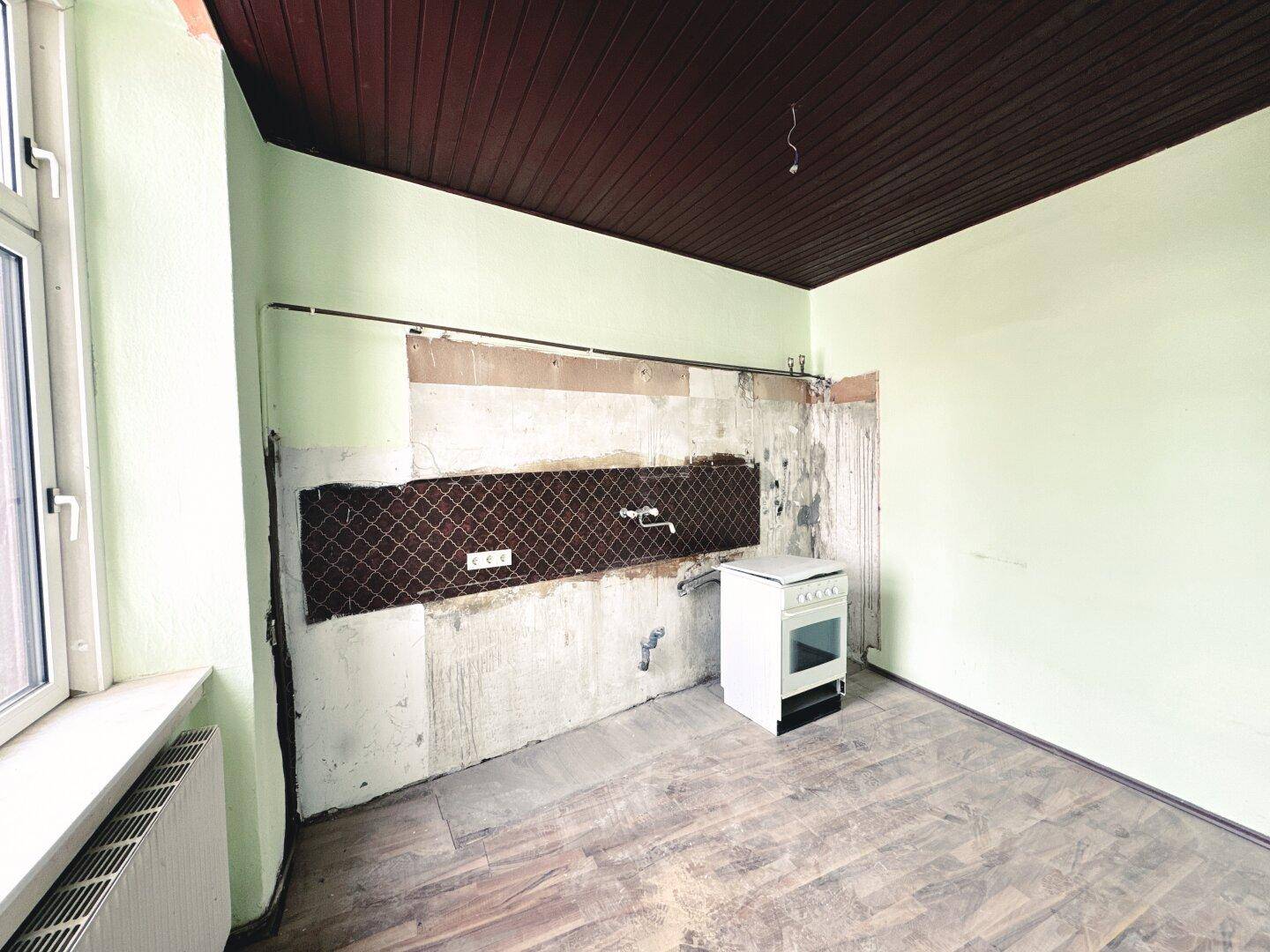 Leere Küche mit freigelegter Wand und Holzdecke, bereit für eine neue Einrichtung.