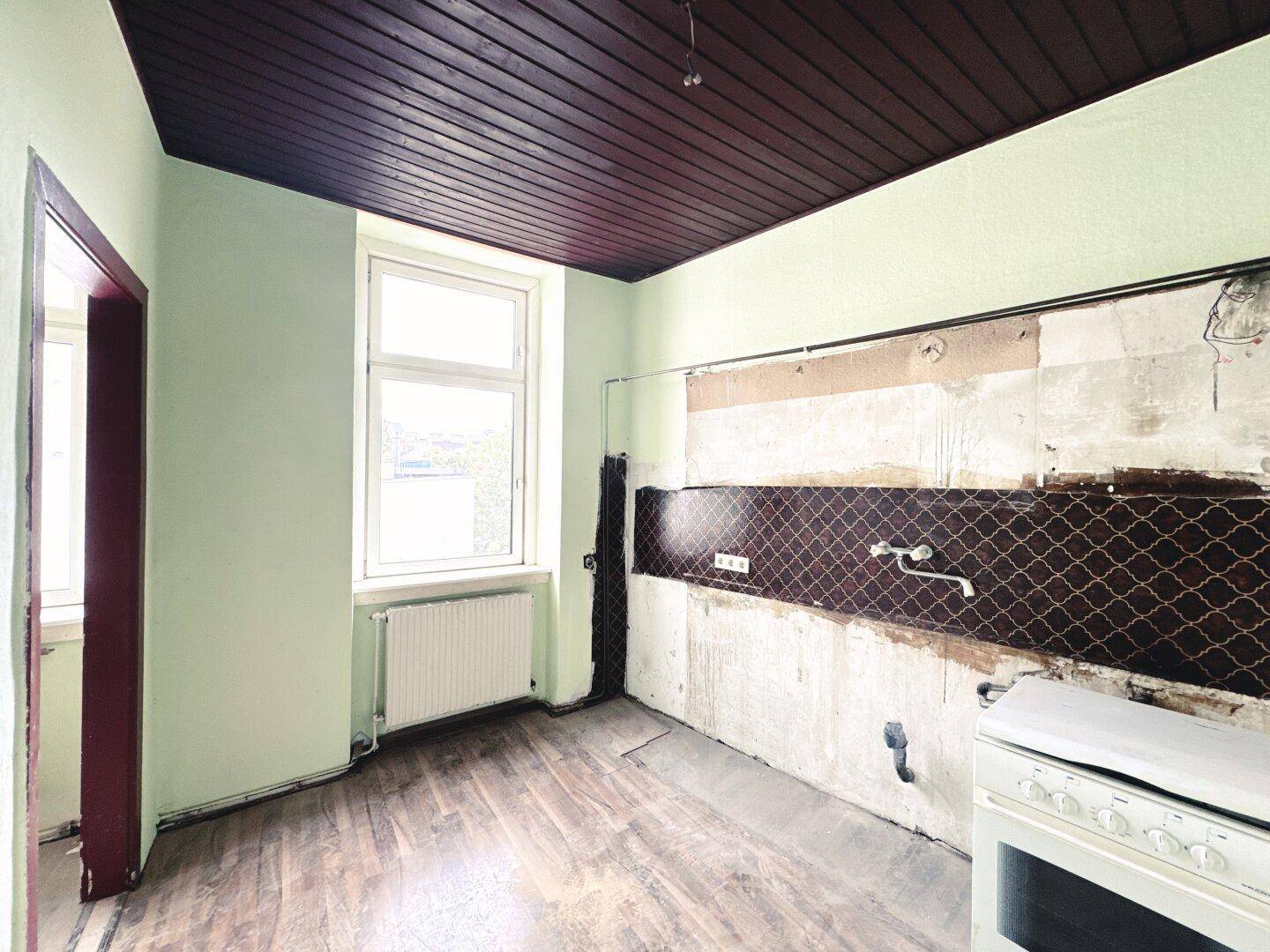 Küche mit freigelegter Wand, Holzdecke und Fenster, wartet auf eine Modernisierung.