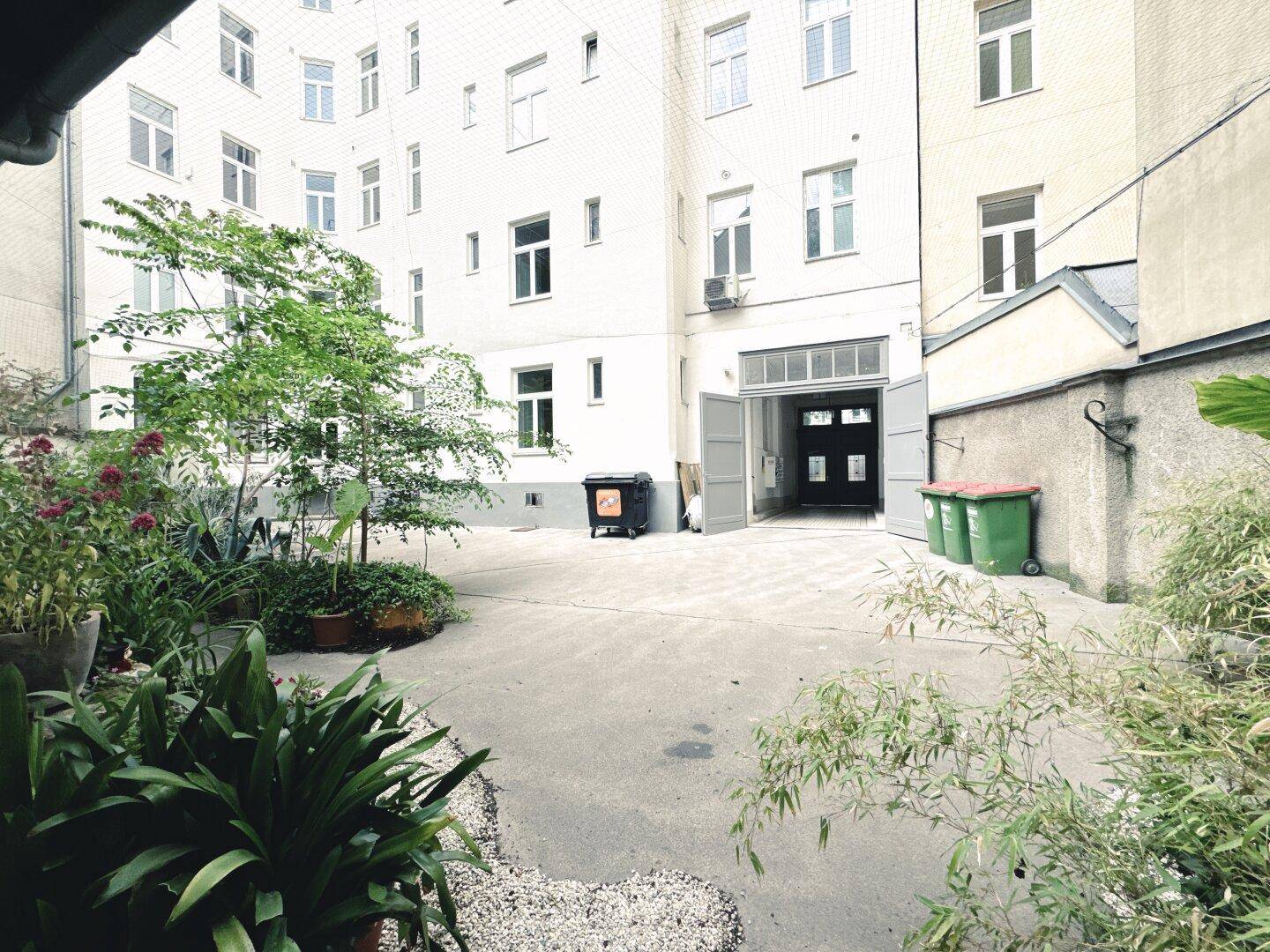Grüner Innenhof mit Pflanzen und Gebäudefassaden, bietet einen ruhigen Rückzugsort.