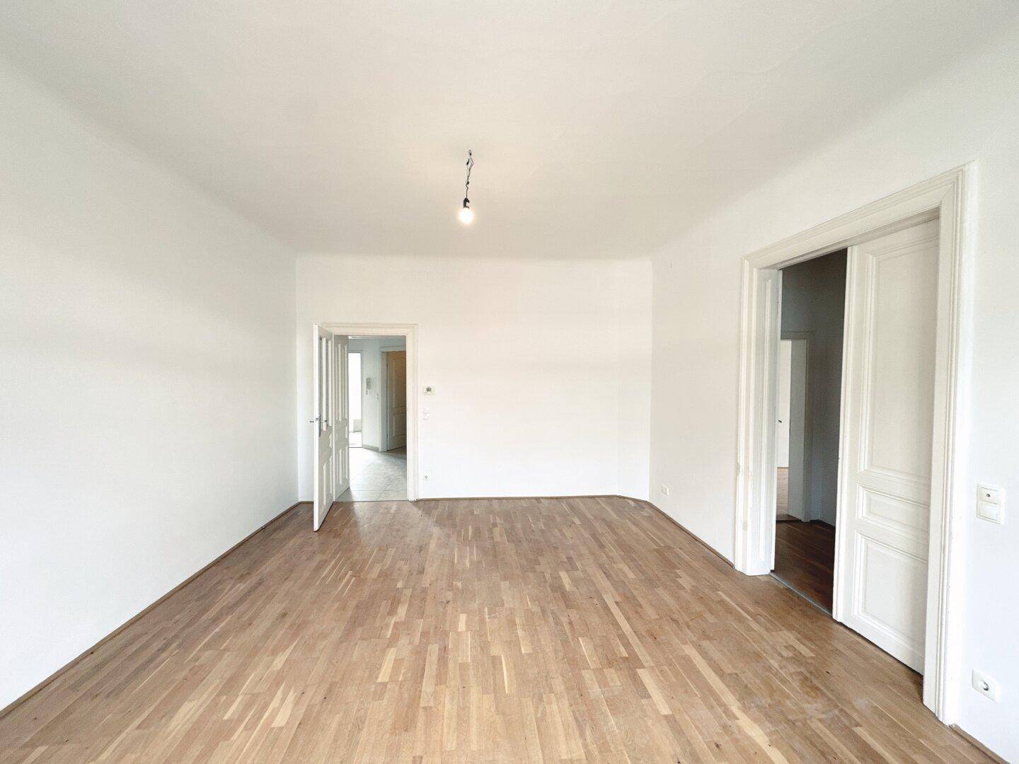 Großes, helles Zimmer mit Parkettboden und mehreren Türöffnungen, bietet vielseitige Nutzungsmöglichkeiten.