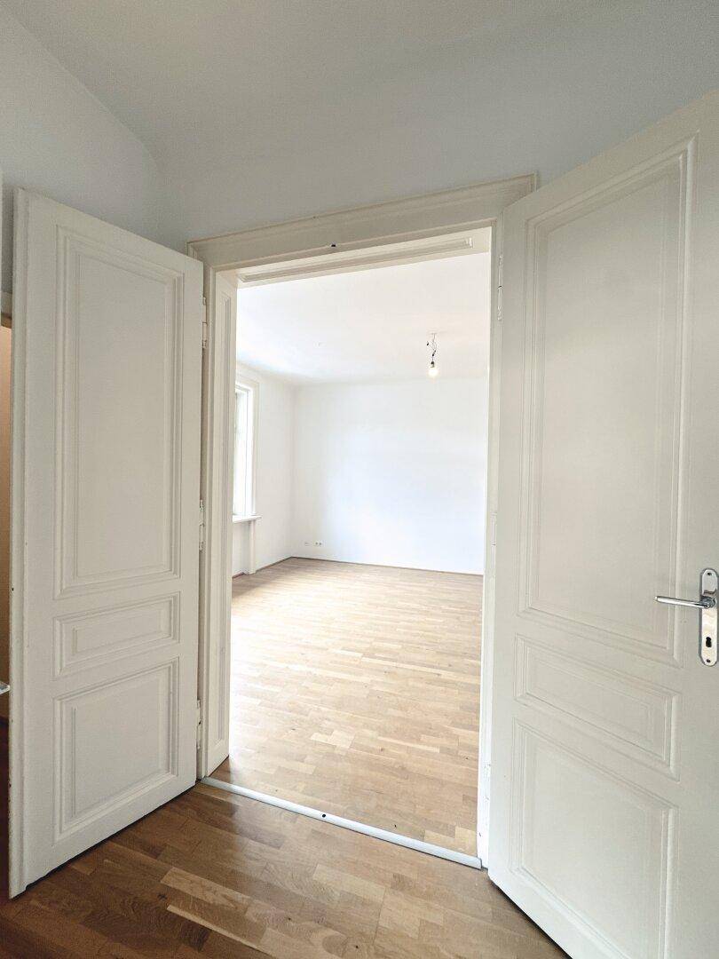 Offene Doppeltür führt in ein helles Zimmer mit Parkettboden, ideal für großzügiges Wohnen.