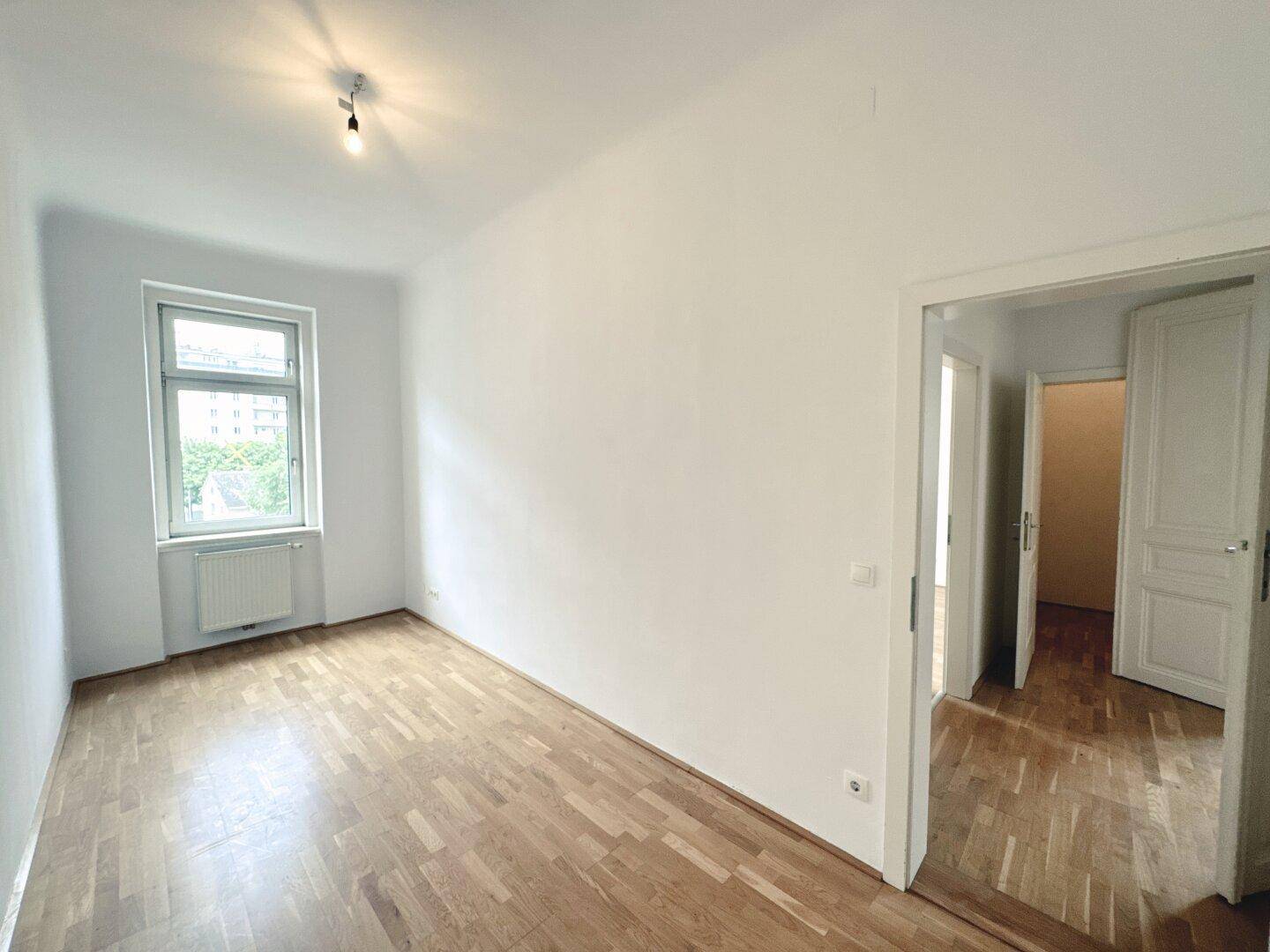 Helles, leeres Zimmer mit Parkettboden und Fenster, geeignet als Schlafzimmer oder Arbeitszimmer.